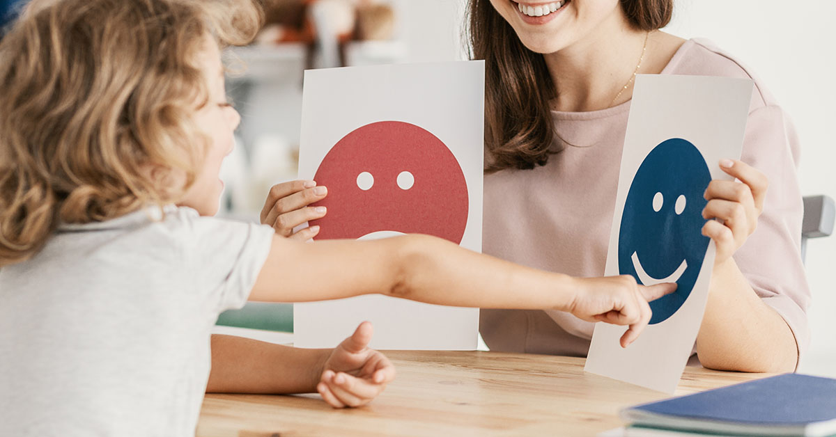 Kivinna håller upp två bilder med glatt och ledset ansikte, barn pekar på den glada.