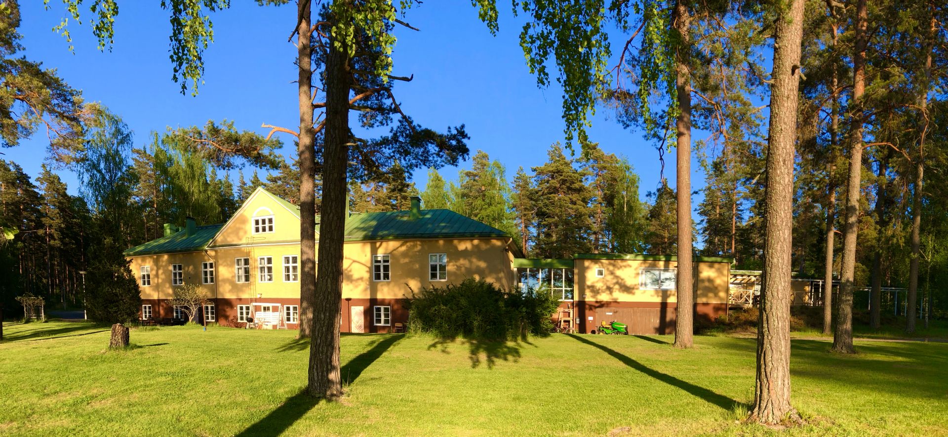 Ett gult hus med gräsplan och träd omkring.