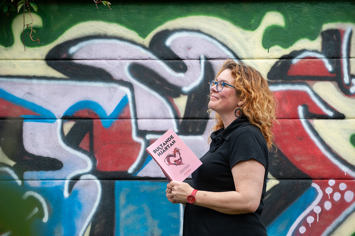 Jolin Slotte med boken Bultande hjärten mot en graffiti vägg.