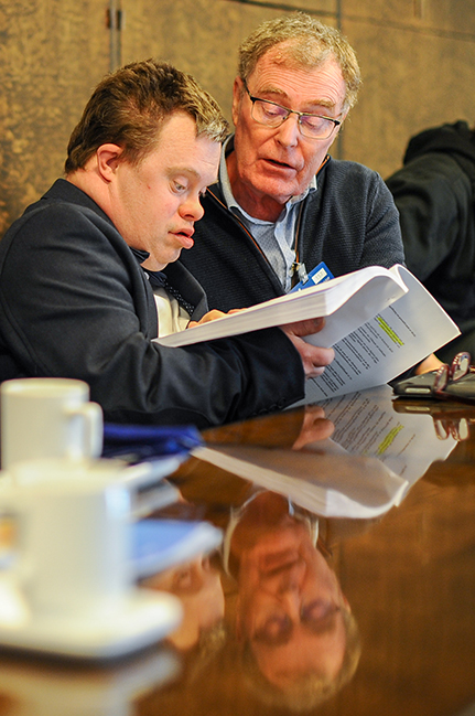 Person med Downs syndrom läser i en hög med papper tillsammans med äldre man.