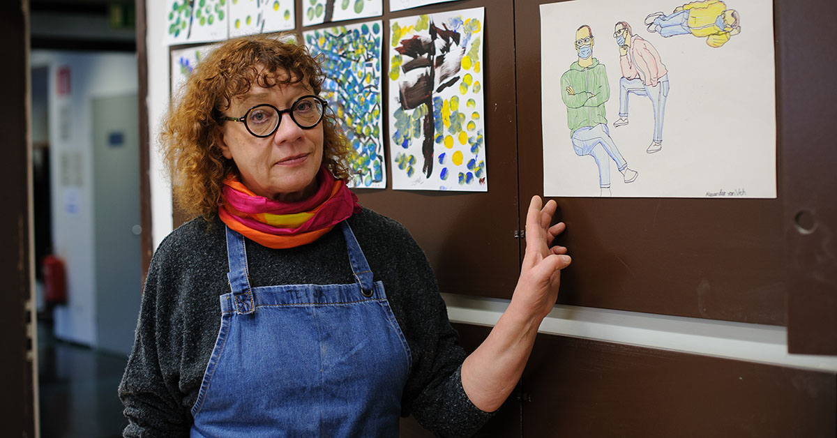 Kvinna med glasögon visar med handen mot målningar på väggen.