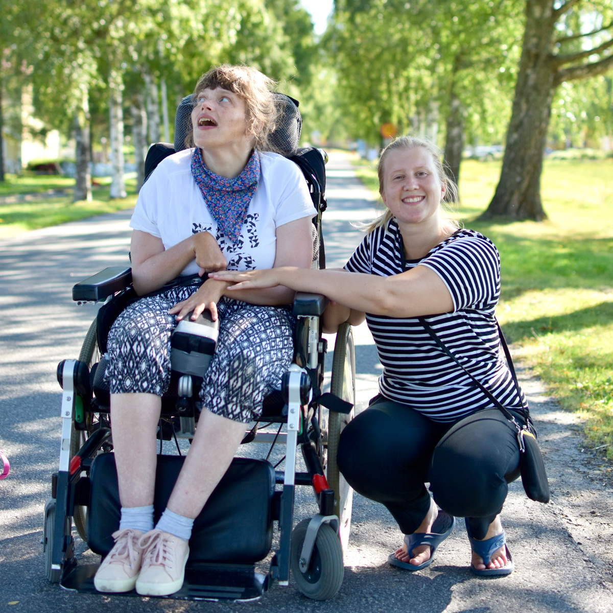 Person i rullstol och bredvid henne står en vårdare på huk