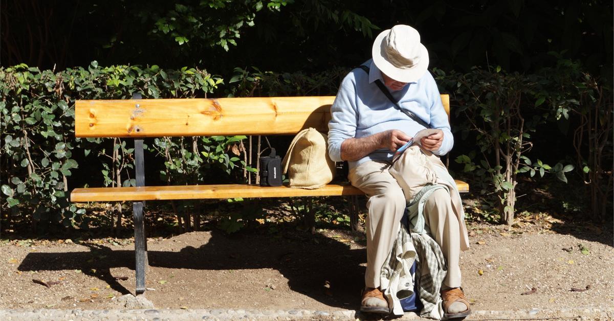 Äldre person sitter på en bänk utomhus och bläddrar bland sina papper