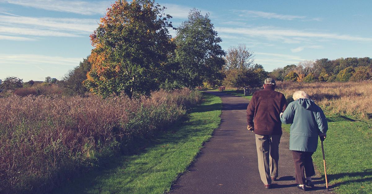 Ett äldre par går armkrok längs en väg i höstigt landskap