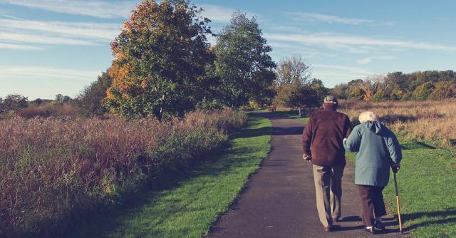 Ett äldre par går armkrok längs en väg i höstigt landskap