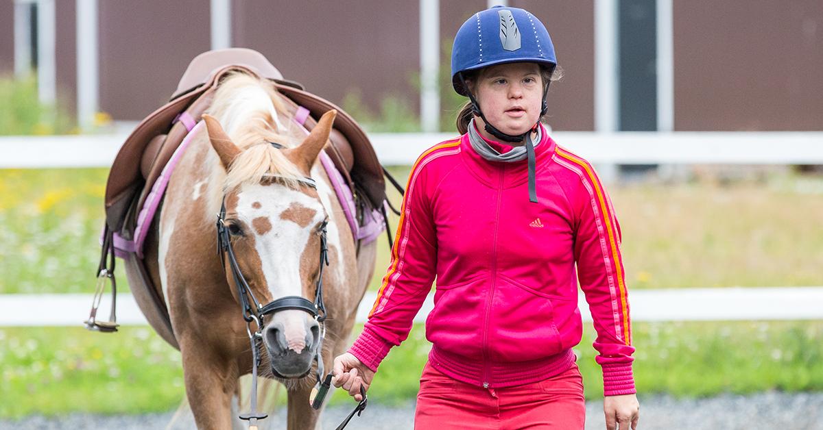 Ung kvinna med Downs syndrom leder en häst.