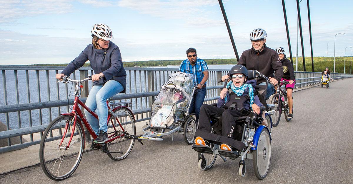 Personer med funktionsnedsättning i olika ålder åker över en bro i specialcyklar.
