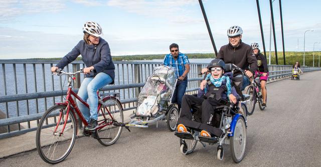 Personer med funktionsnedsättning i olika åldrar och anhörgia tar sig över en bro i olika specialcyklar.