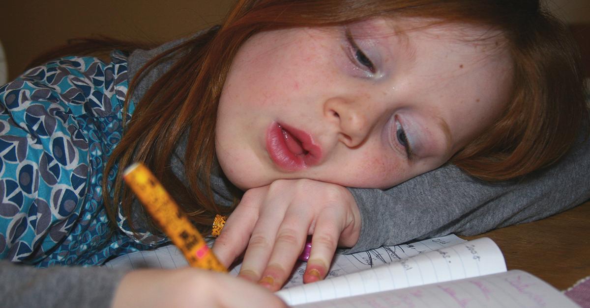 En trött flicka som gör sina läxor.