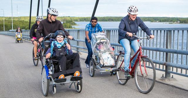 Flera personer cyklar med special hjälpmedel över en bro.