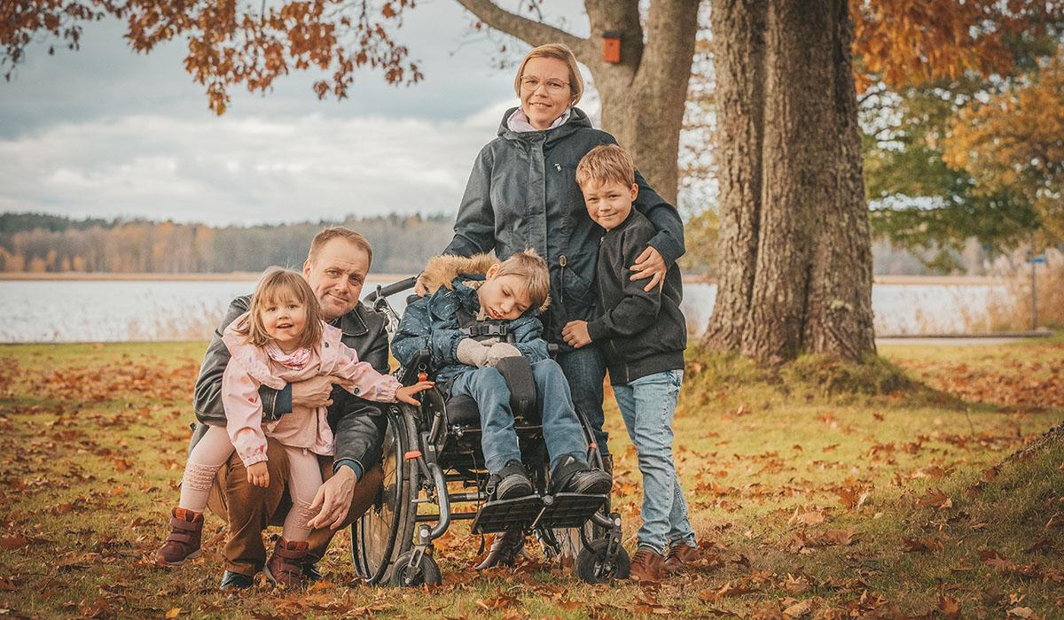 Två vuxna och tre barn varav ett i rullstol i vacker höstmiljö.