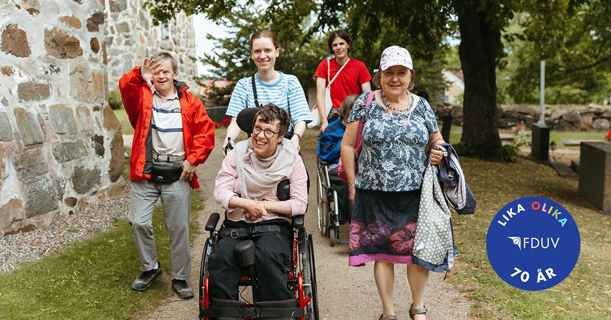 Personer med funktionsnedsättning och personal på promenad i somrig miljö.