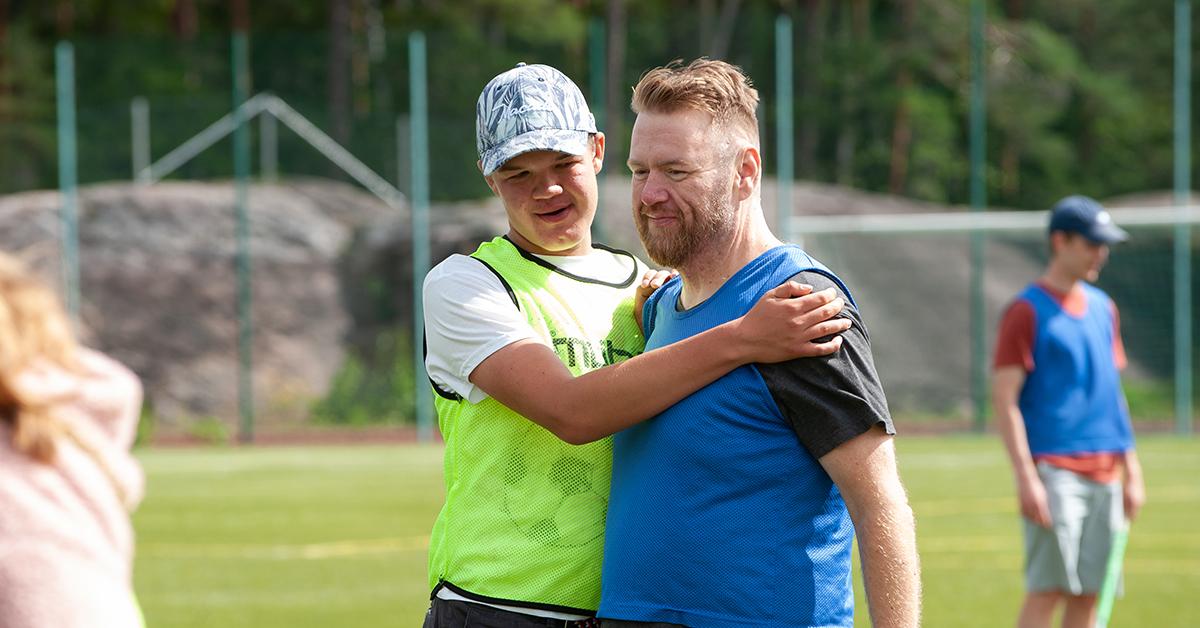 En kille med keps och gul väst håller om en man.